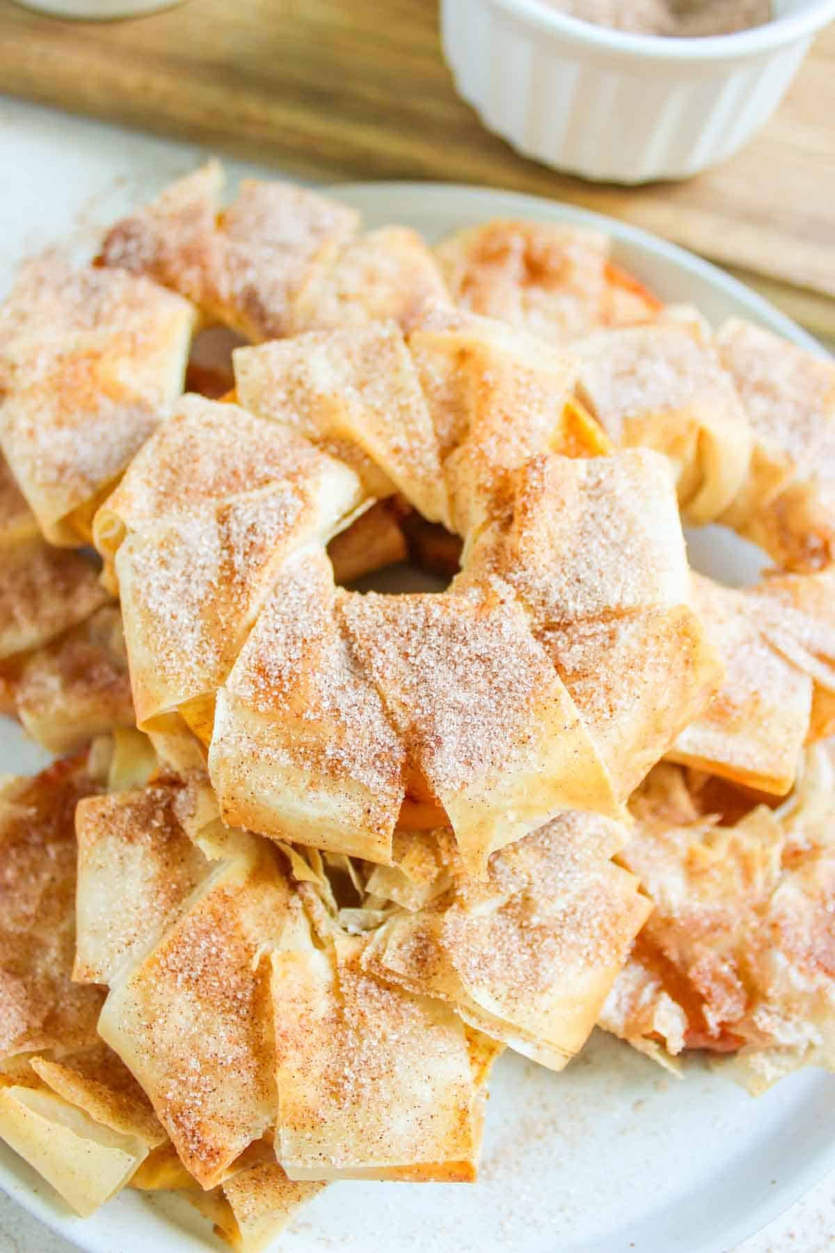 A plate of cinnamon sugar-coated pastry pieces, resembling delectable Cinnamon Apple Strudel slices, arranged in a ring shape on a neutral-colored plate.