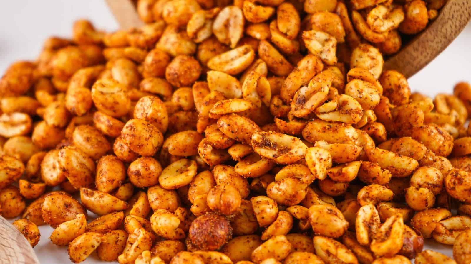 Close-up of a pile of spicy, seasoned peanuts, with some spilling from a wooden bowl in the background.