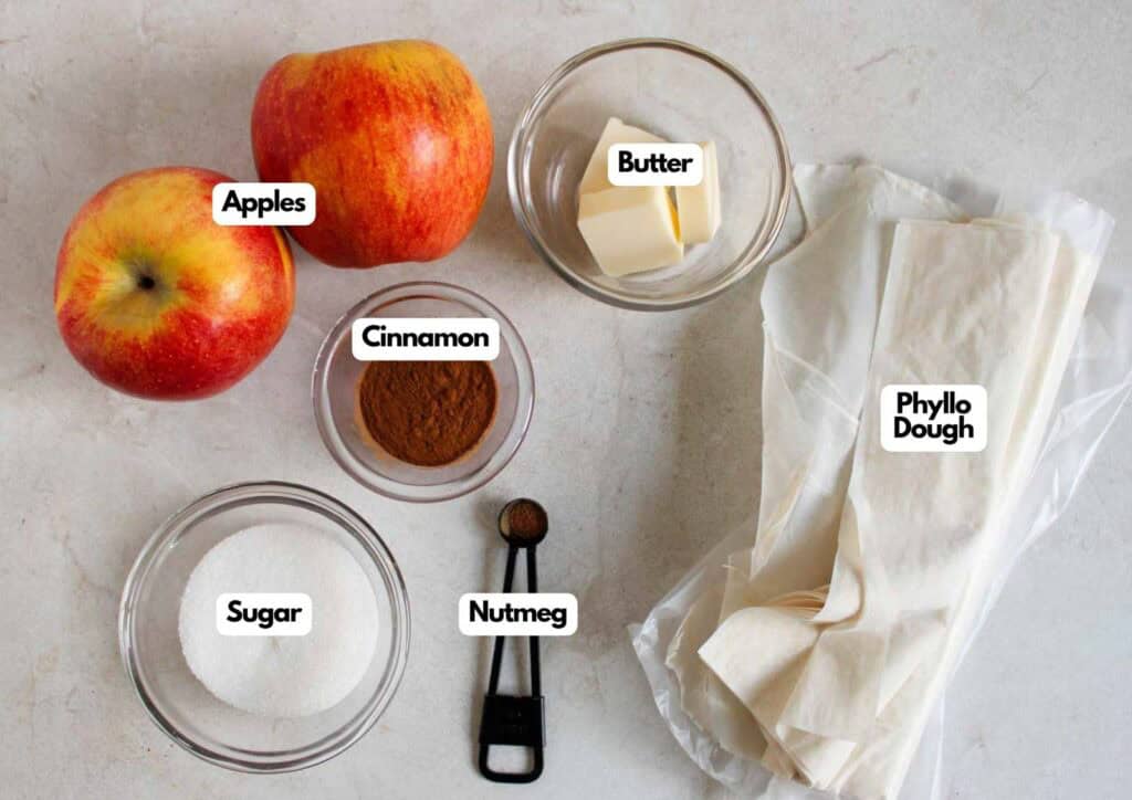 Apple strudel ingredients laid out including fresh apples, phyllo dough, butter, sugar, cinnamon, and nutmeg