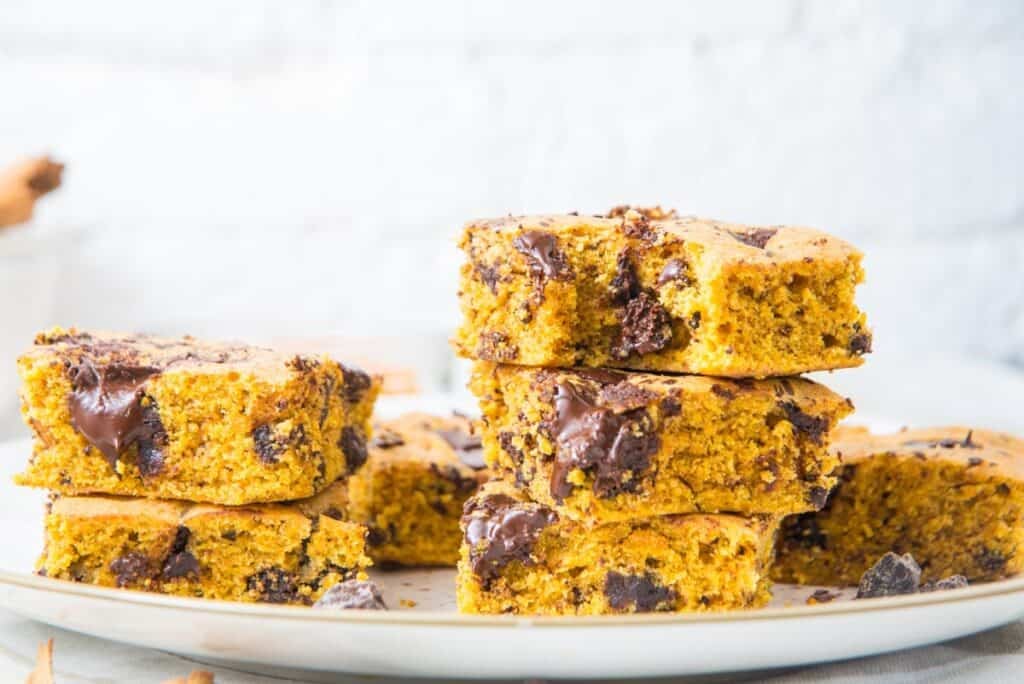 Stack of homemade pumpkin bars with melted chocolate chunks on a white plate