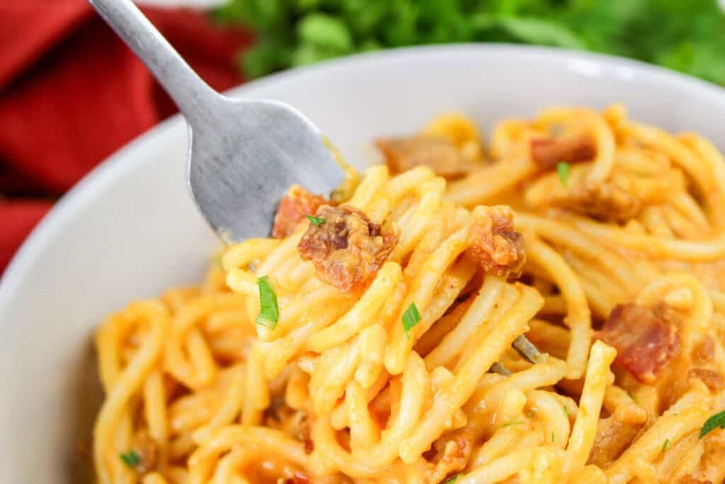 Creamy pumpkin carbonara spaghetti with crispy bacon pieces and fresh parsley garnish on a white plate