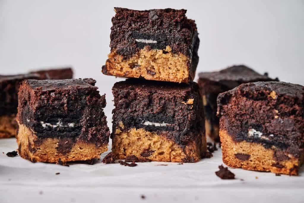 Stack of slutty brownies showing layers of chocolate chip cookie dough, Oreo cookies, and fudgy brownie