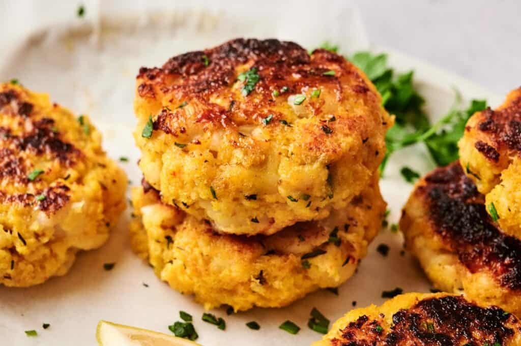 Stack of golden pan-fried Maryland crab cakes garnished with fresh chopped parsley and lemon wedge on a white plate