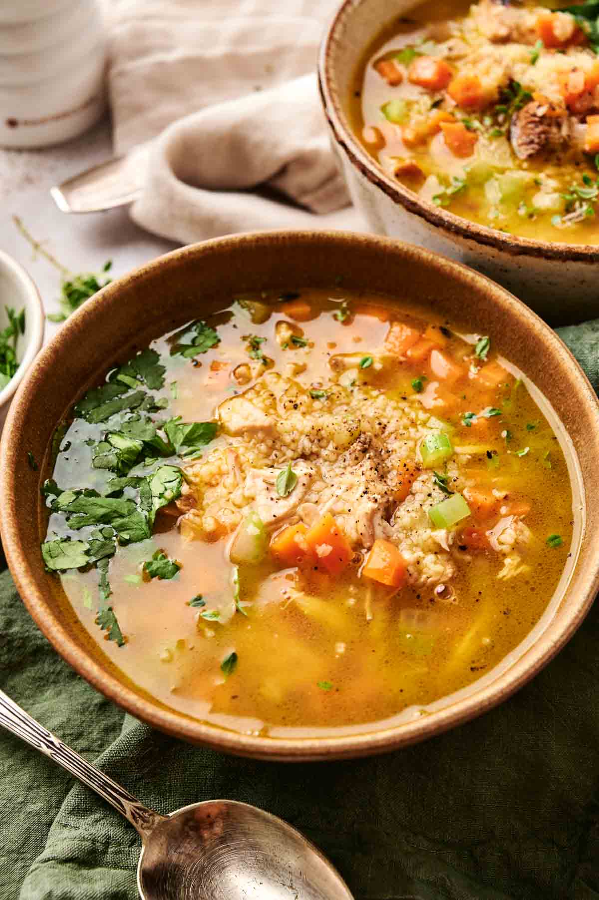 A comforting bowl of turkey soup featuring carrots, celery, and herbs, with a spoon and napkin nearby.