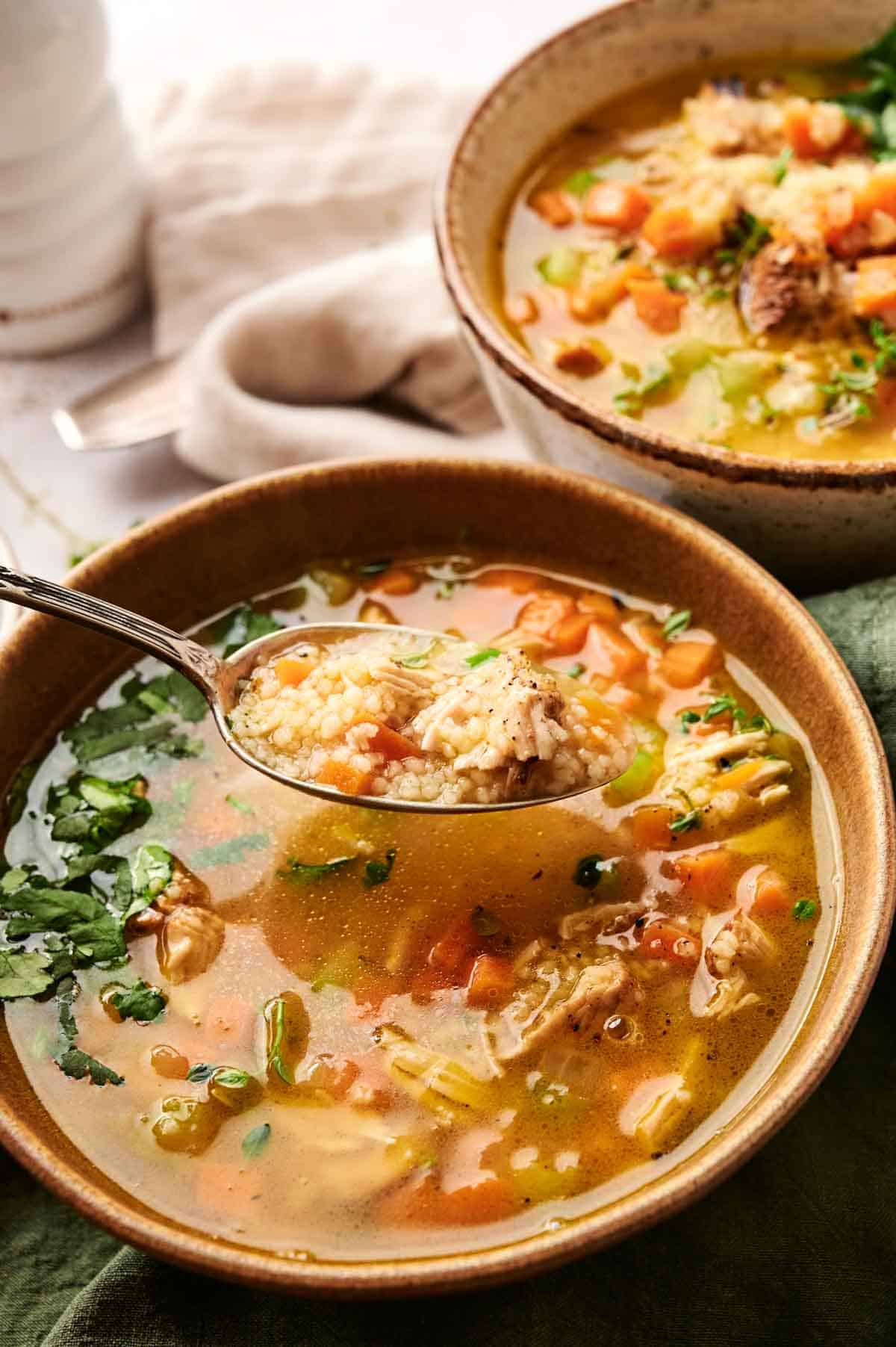 Two bowls of turkey and rice soup with vegetables. A spoon lifts a portion from one bowl.