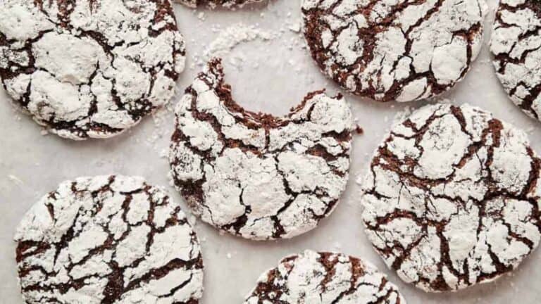 Chocolate crinkle cookies with a powdered sugar coating, one has a bite taken out of it.