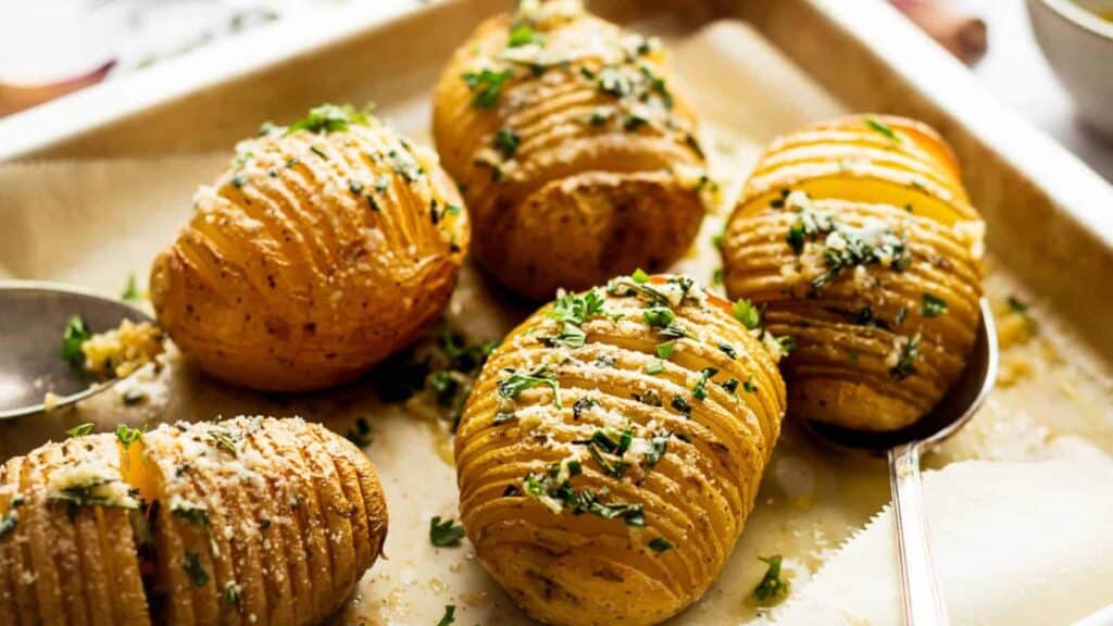 Hasselback potatoes with herbs and grated cheese on a baking sheet.