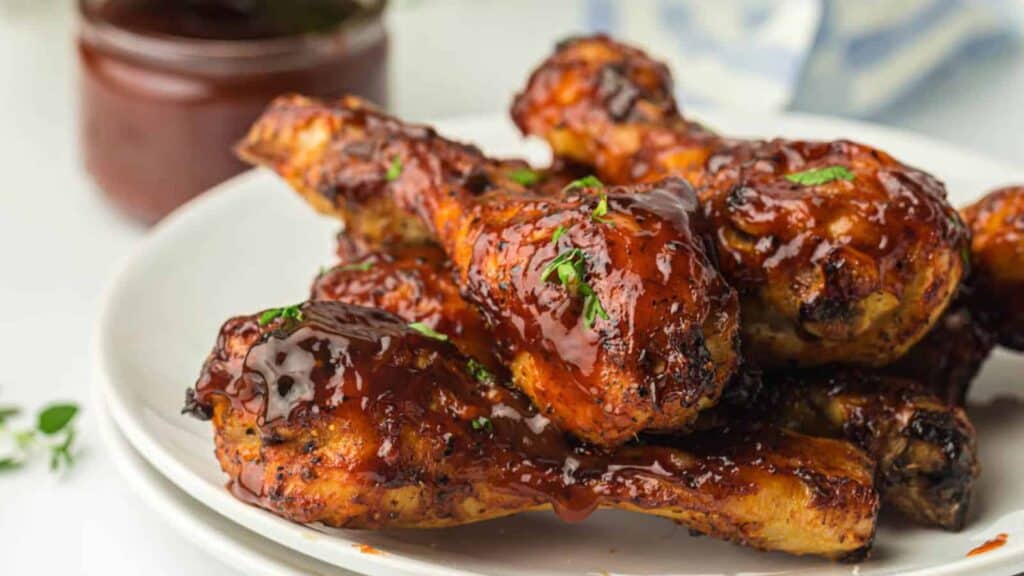 A plate of glazed barbecue chicken drumsticks garnished with herbs.