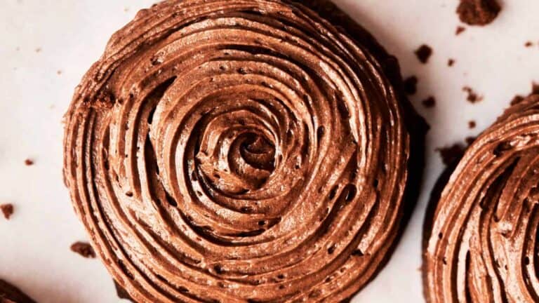 Close-up of a chocolate frosting swirled on a round baked good, with some crumbs scattered around.