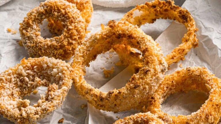A close-up of crispy, golden-brown onion rings on parchment paper.