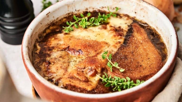 A close-up of baked French onion soup topped with melted cheese and garnished with fresh thyme in a rustic bowl.