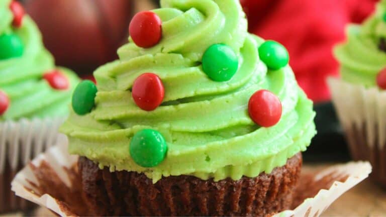 A chocolate cupcake with green frosting swirled on top, decorated with red and green candy pieces, in a paper liner.