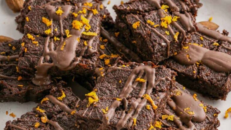 A stack of chocolate brownies topped with chocolate drizzle and orange zest, arranged on a white plate.