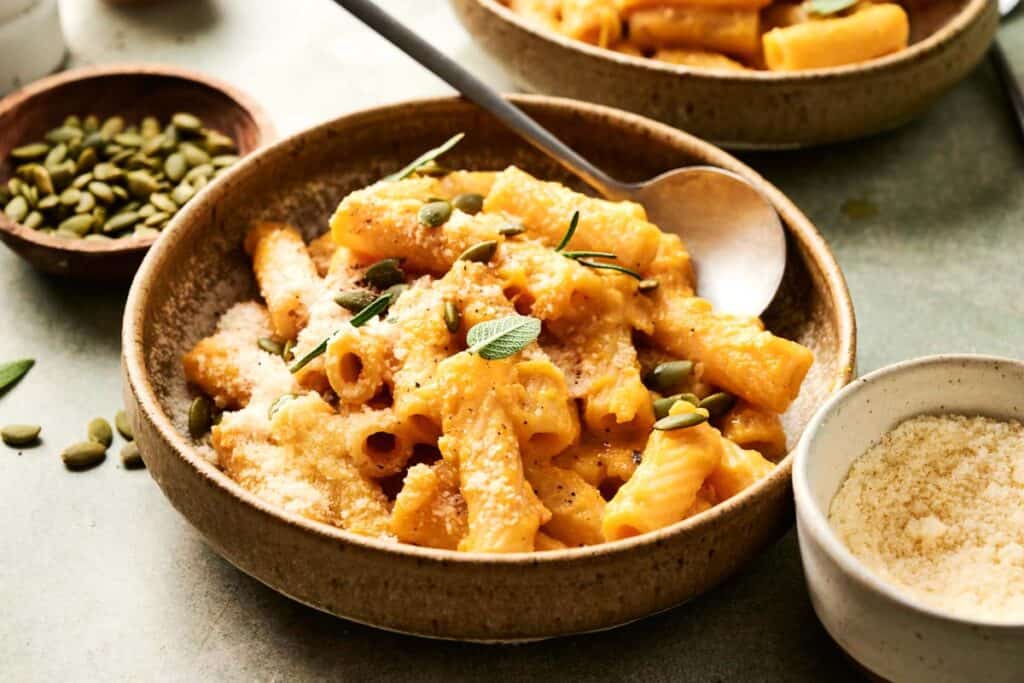 Penne pasta in creamy pumpkin sauce topped with toasted pumpkin seeds and fresh sage leaves, served in a bowl