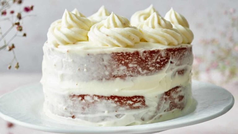 A two-layer cake with partially visible red layers and white frosting, topped with decorative frosting swirls, on a white plate.