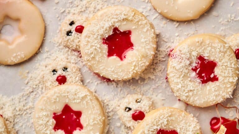 Cookies with red star-shaped centers, white icing, and coconut shreds on top are laid out on a surface.