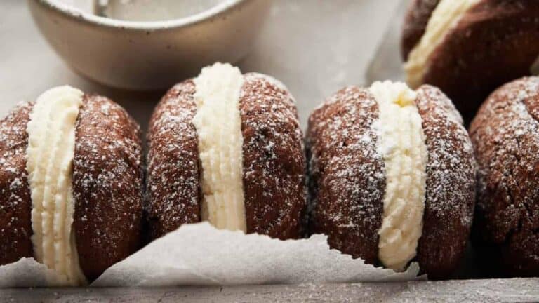 Chocolate pastries with cream filling on parchment paper, lightly dusted with powdered sugar, with a bowl in the background.