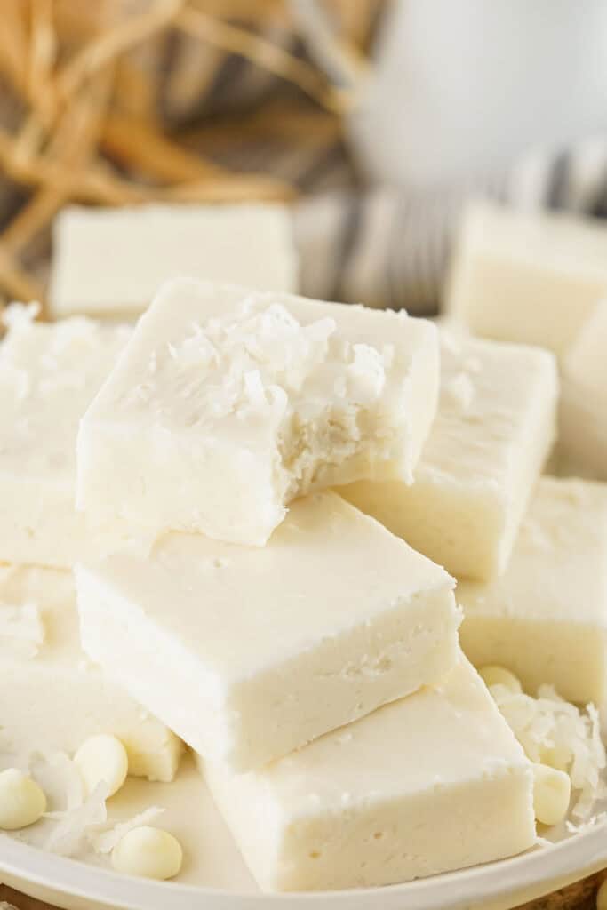 A stack of coconut fudge pieces, rich and creamy, topped with delicate shreds of white chocolate on a plate.
