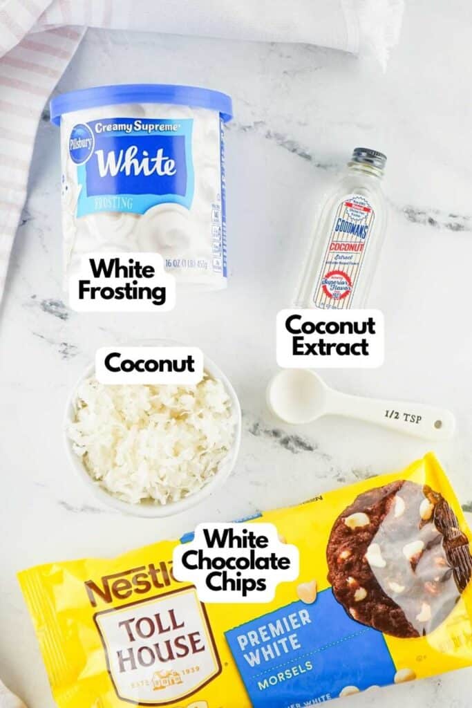 Ingredients for a coconut fudge recipe are laid out on a table: white frosting, coconut extract, shredded coconut, white chocolate chips, and a half teaspoon measuring spoon.