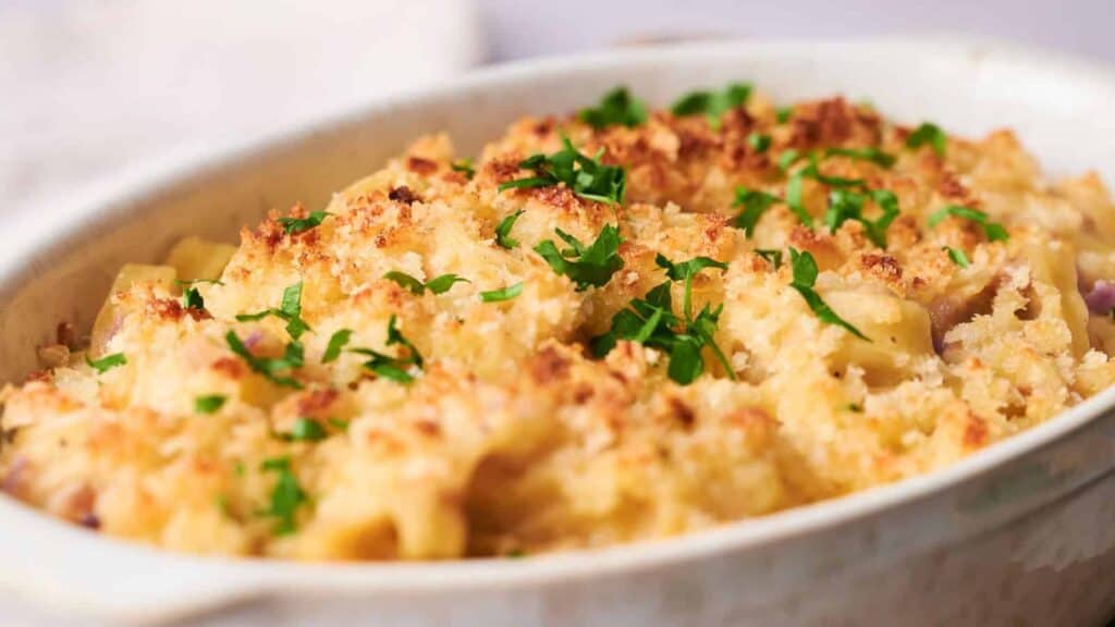 A baked macaroni and cheese dish topped with breadcrumbs and garnished with chopped parsley in a white oval dish.