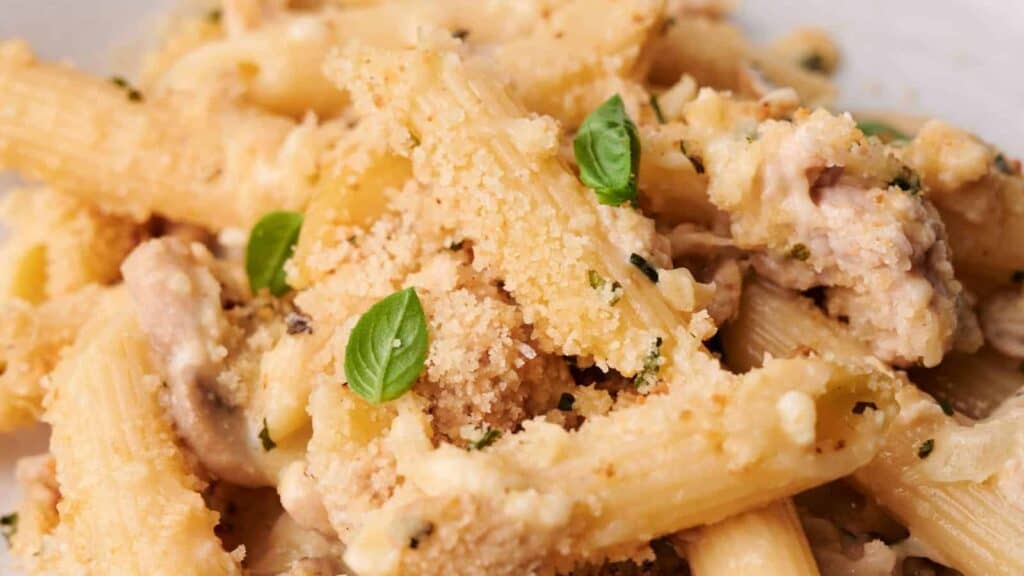 Close-up of creamy pasta with mushrooms, bread crumbs, and fresh basil leaves.
