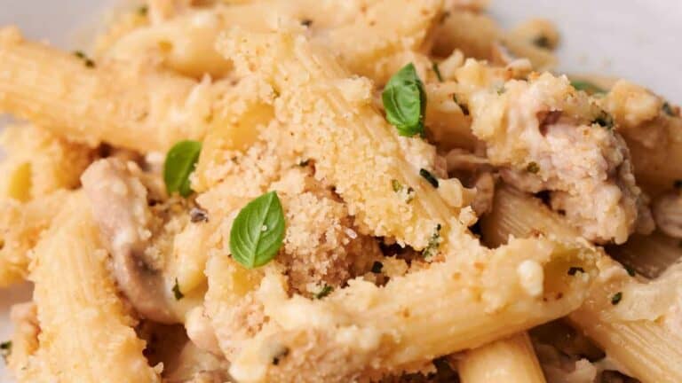 Close-up of creamy pasta with mushrooms, bread crumbs, and fresh basil leaves.