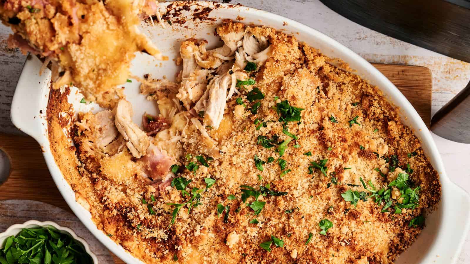 Baked breadcrumb-topped casserole with pieces of chicken, garnished with chopped parsley in a white dish.