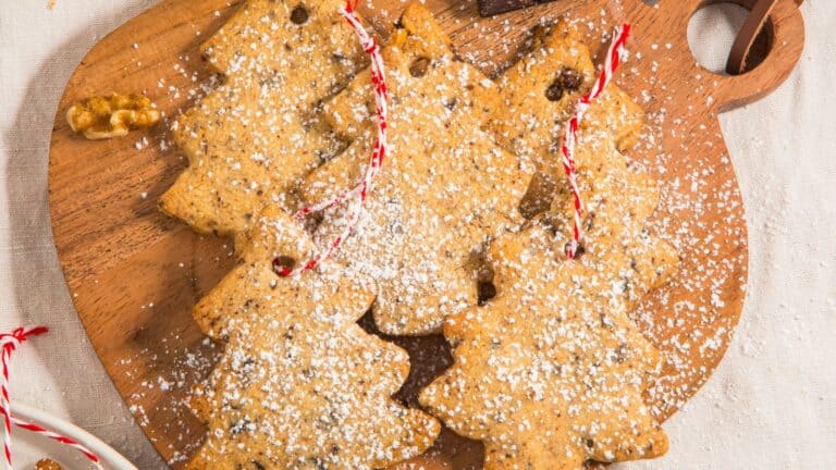 Tree-shaped cookies dusted with powdered sugar on a wooden cutting board, with bits of red and white string.