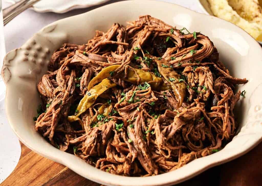 Bowl of shredded Mississippi pot roast with pepperoncini peppers and fresh herbs