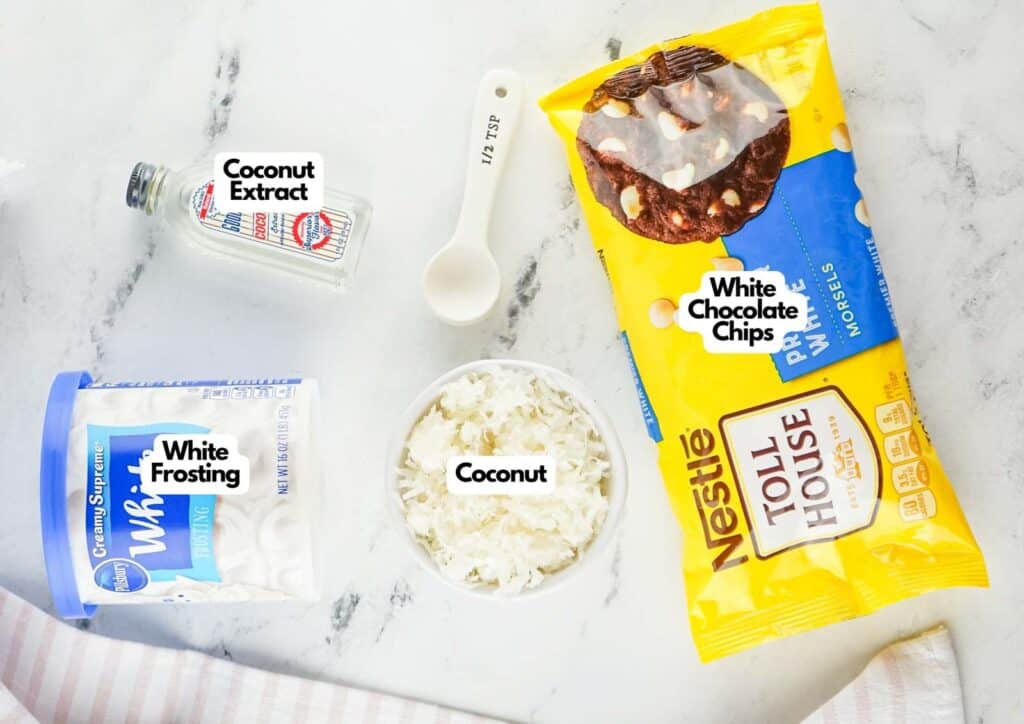 Coconut fudge ingredients laid out on a marble surface including Nestl&eacute; Toll House white chocolate chips, shredded coconut, Pillsbury white frosting, and coconut extract