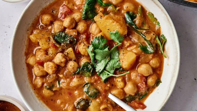 A bowl of chickpea curry with potatoes, spinach, and cilantro garnish.