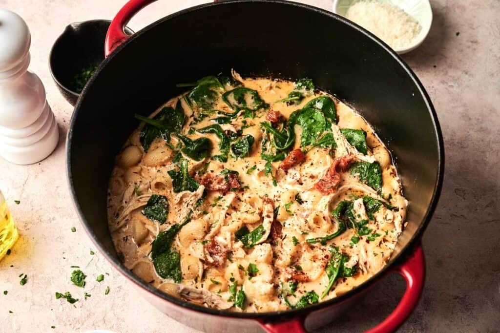 Marry me chicken soup simmering in a pot, with shell pasta, wilted spinach, and sun-dried tomatoes in a creamy broth