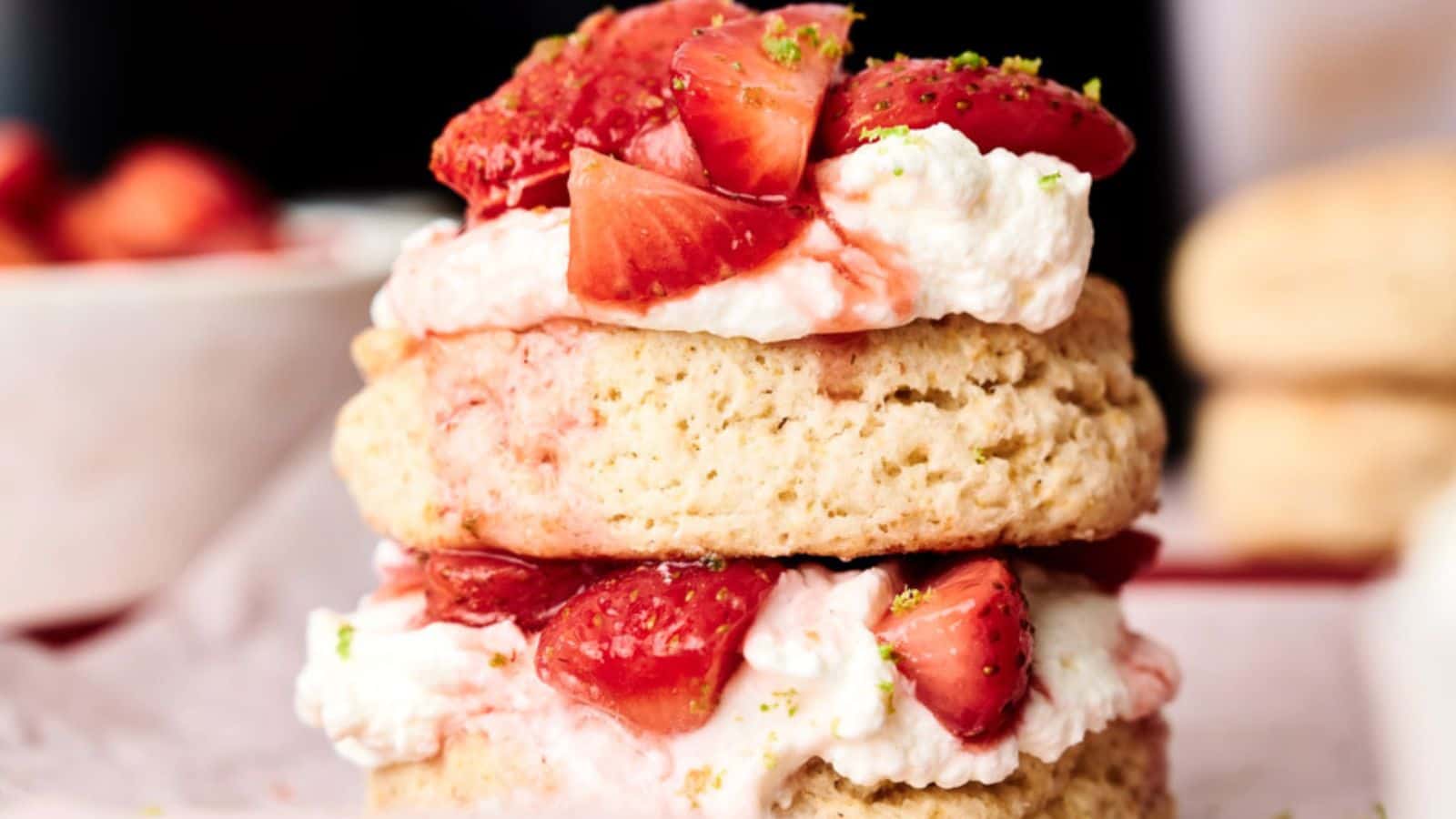 Two layers of biscuit with cream and sliced strawberries in between, topped with more strawberries and a sprinkle of green zest.