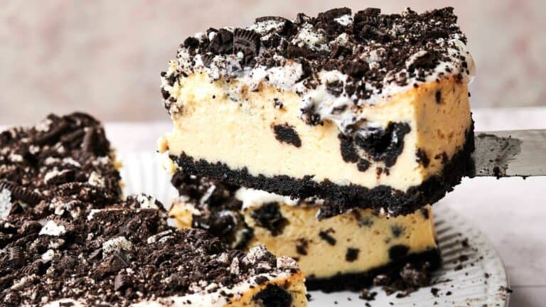 A slice of Oreo cheesecake being served on a spatula, featuring a crumbly Oreo crust, creamy cheesecake filling with Oreo pieces, and a topping of crushed Oreos.