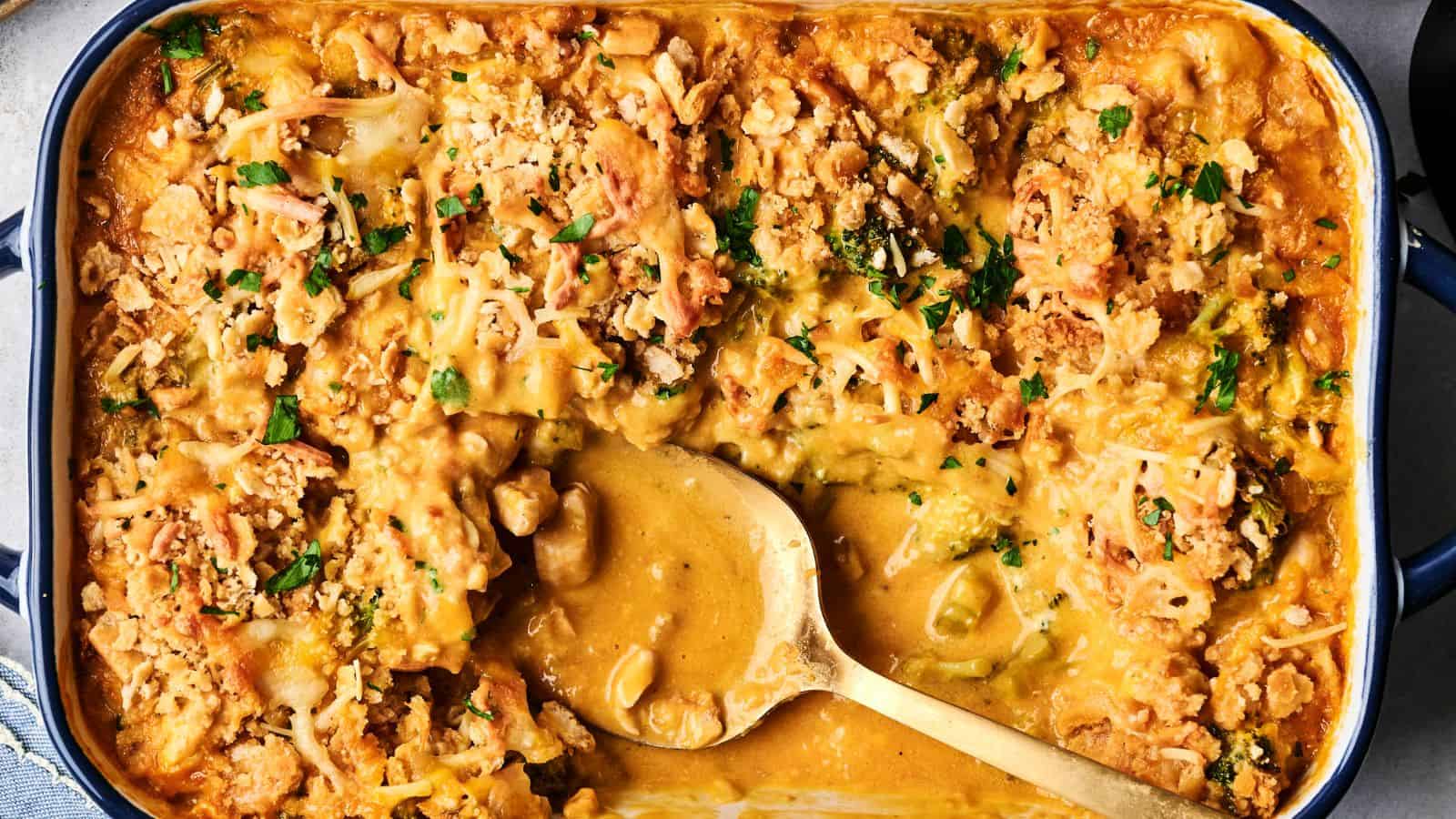 A baked casserole in a dish with a golden breadcrumb and cheese topping, featuring a serving spoon. Garnished with chopped herbs.