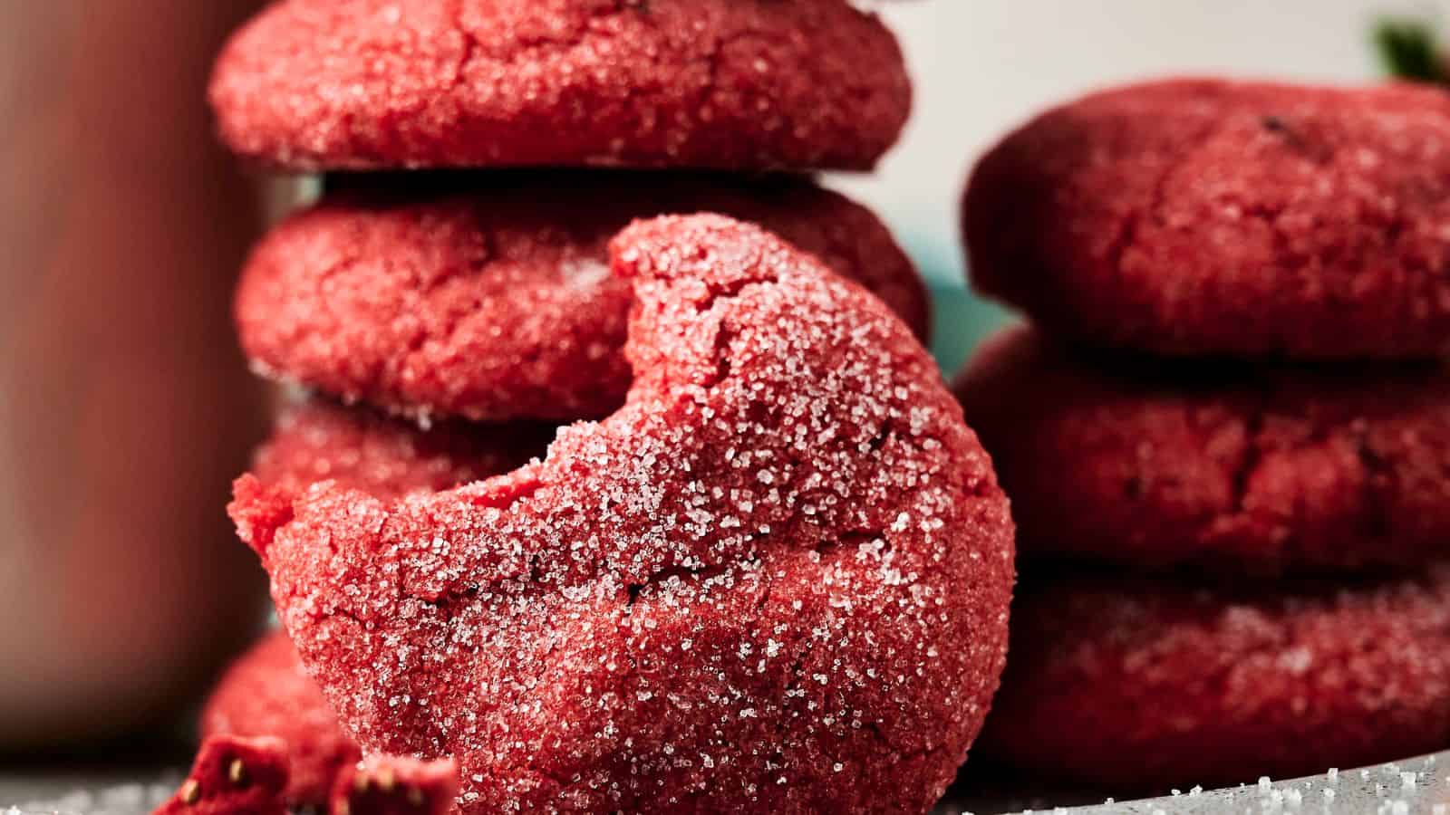 Close-up of red cookies coated in sugar, with one cookie in the foreground showing a bite taken out of it.
