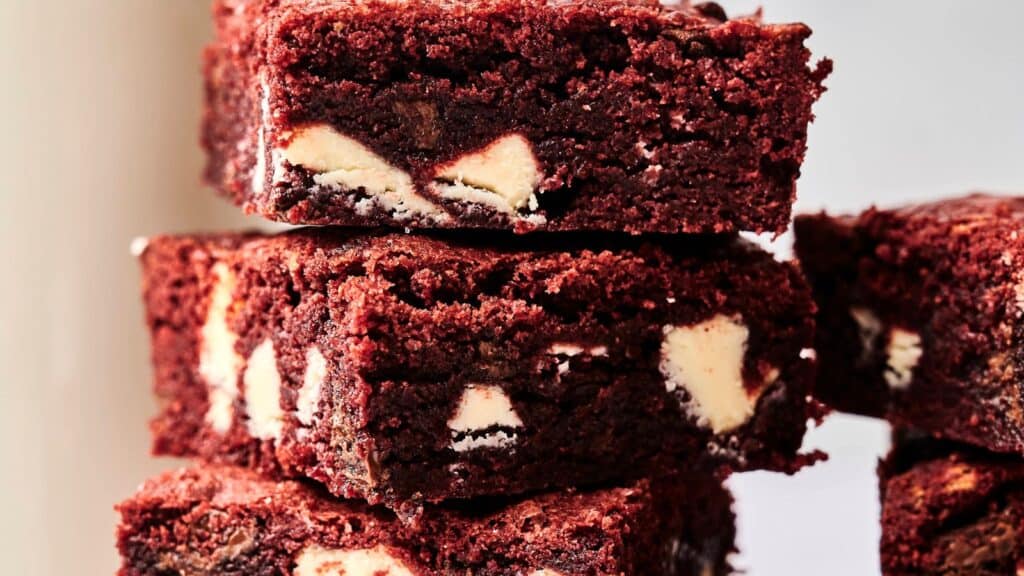 Close-up of a stack of red velvet brownies with white chocolate chunks against a neutral background.