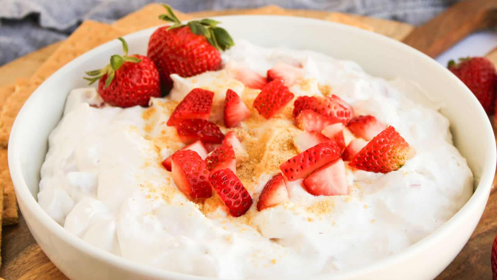A white bowl filled with creamy dip topped with chopped fresh strawberries and a light sprinkle of crumbs.