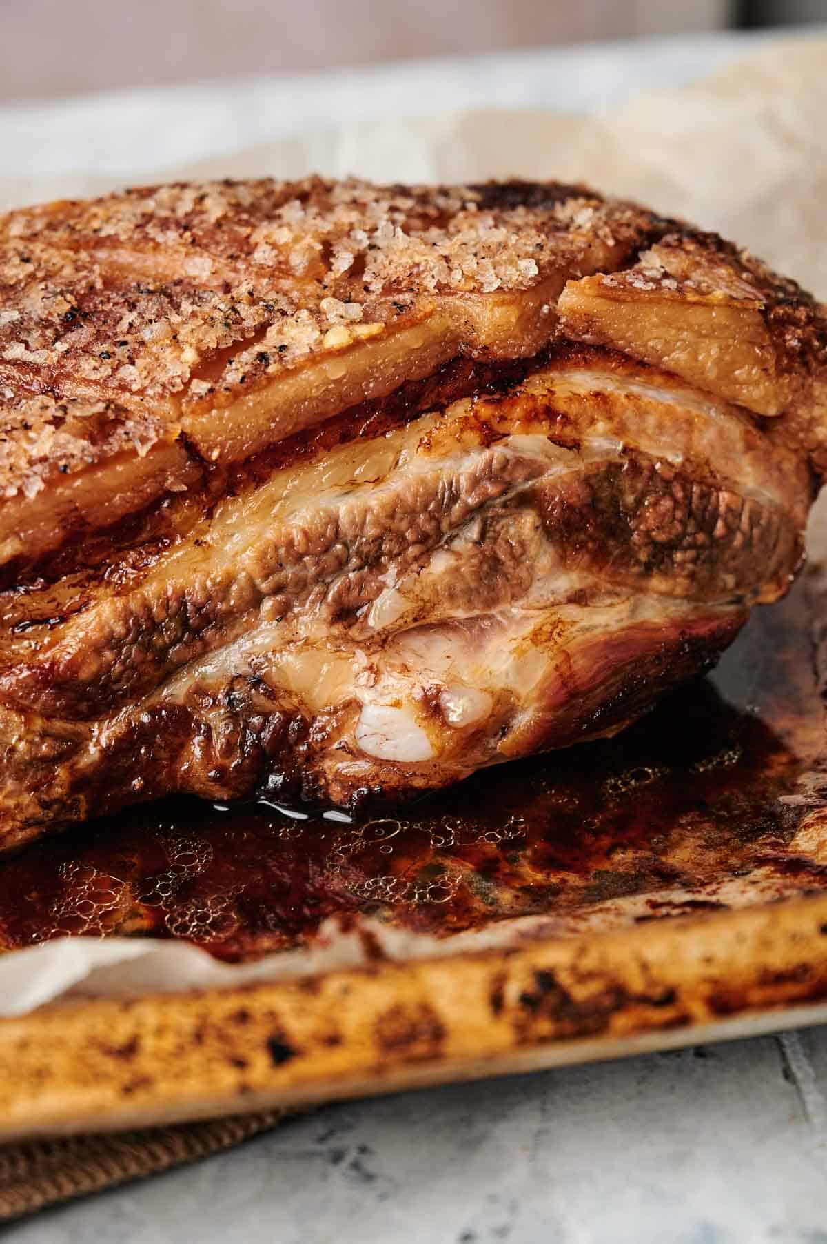 Close-up of a cooked, seasoned piece of pork belly with a crispy, golden-brown crust, resting on a baking sheet lined with parchment paper.