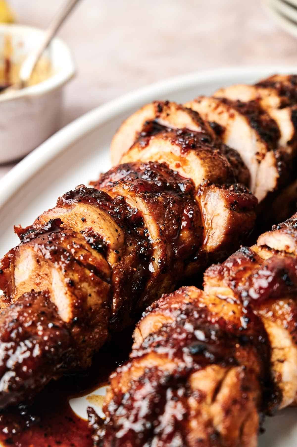 Sliced pork tenderloin with a dark, glossy glaze is artfully arranged on a white platter.