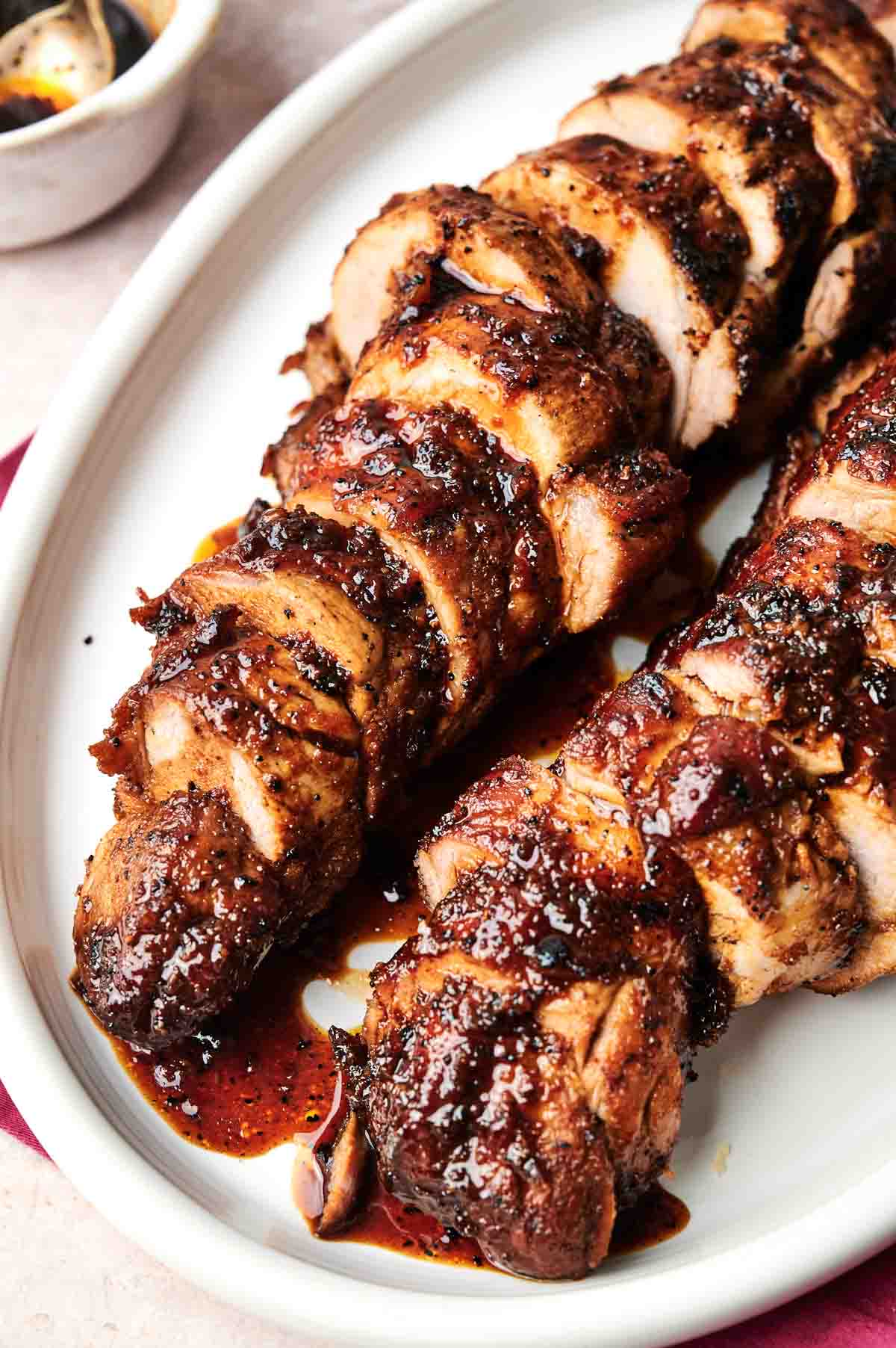 Sliced, glazed pork tenderloin arranged on a white oval plate, showcasing the flavorful seasoning and rich sauce.