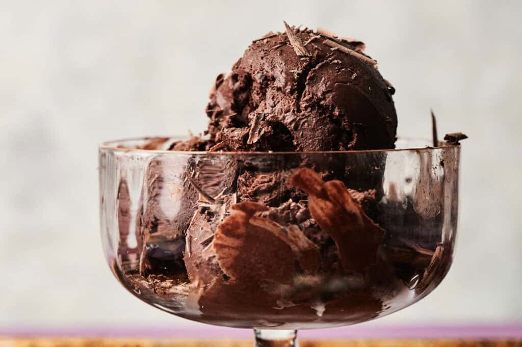 Two scoops of rich homemade dark chocolate ice cream topped with chocolate shavings, served in a clear glass dessert bowl