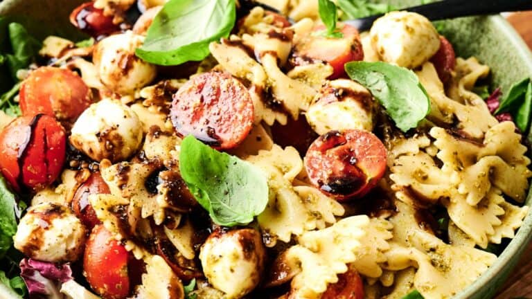 A bowl of bowtie pasta salad with cherry tomatoes, mozzarella balls, fresh basil leaves, and balsamic glaze.