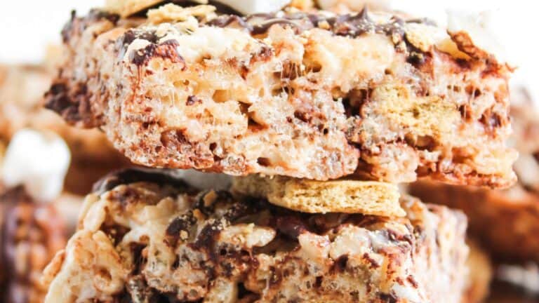 Close-up of stacked dessert bars made with crispy cereal, marshmallows, chocolate drizzle, and graham cracker pieces.