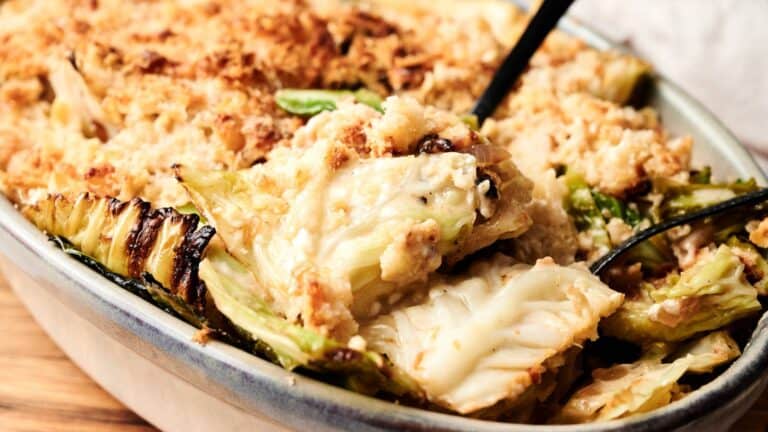 A close-up of a baked cabbage casserole with a breadcrumb topping, showing a serving being scooped out with a spoon.