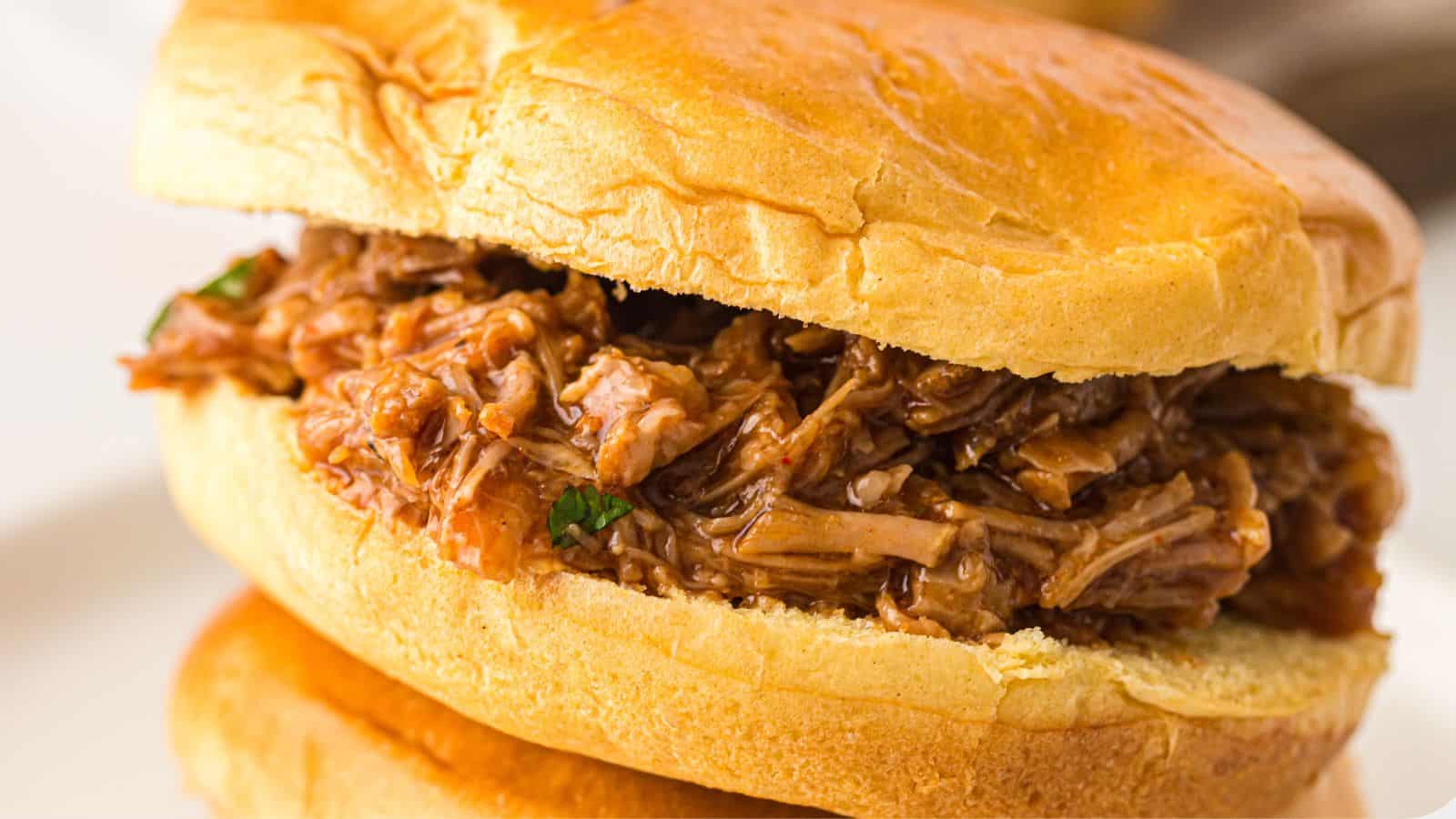 A close-up of a pulled pork sandwich on a soft bun, filled with shredded, saucy pork.