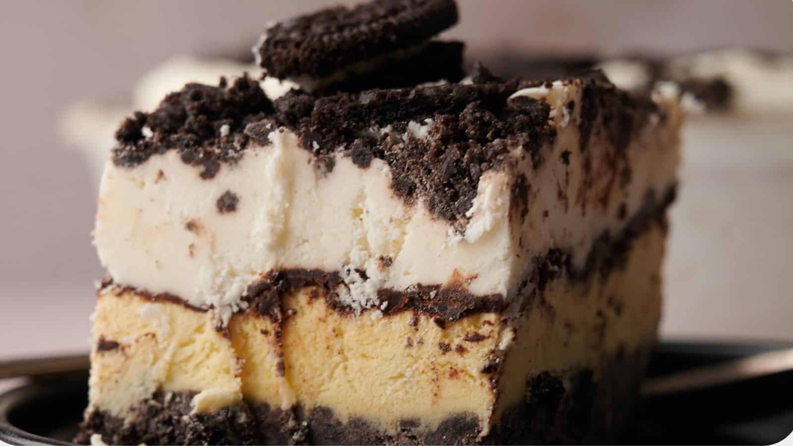 A slice of layered ice cream cake with chocolate cookie crumbles and a cookie on top, served on a plate.