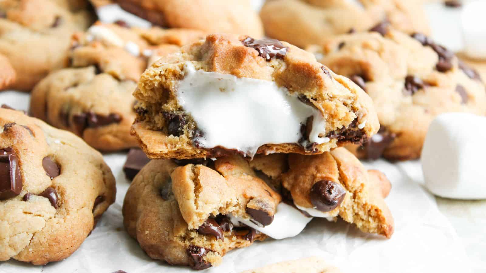 A close-up of chocolate chip cookies filled with melted marshmallow, with one cookie broken open to show the gooey center.