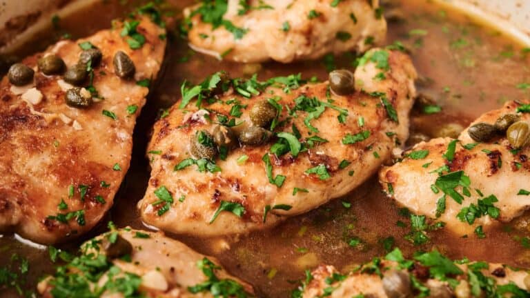 Cooked chicken breasts in a sauce, garnished with chopped parsley and capers.