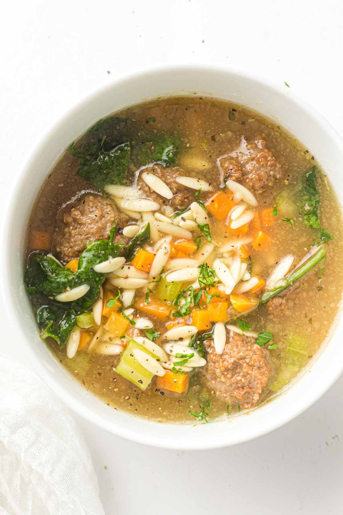 A bowl of Slow Cooker Italian Wedding Soup with meatballs, orzo pasta, chopped carrots, celery, kale, and black pepper in a clear broth.